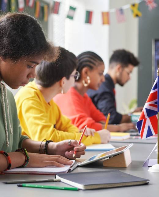 Side view at diverse group of students sitting at table with country flags during international conference in school